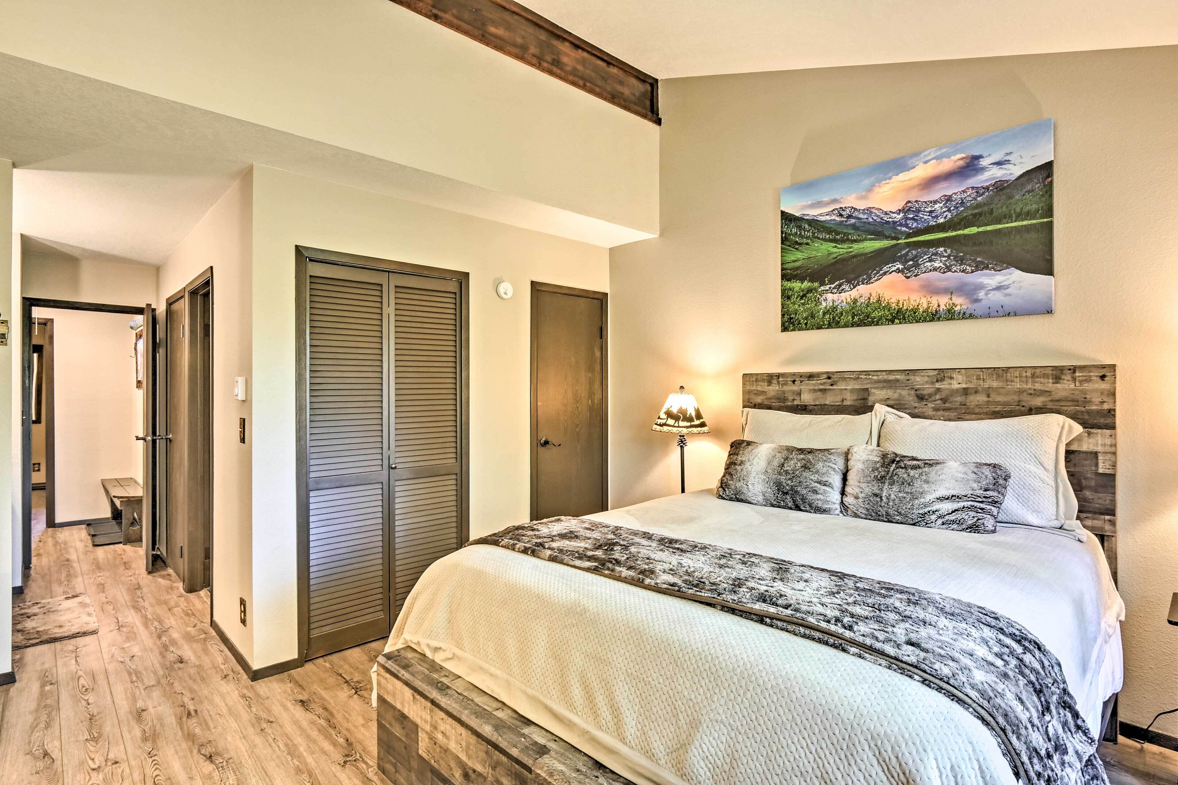 A bedroom with a large bed, a wooden headboard, a painting of a landscape, and a bench in the hallway.