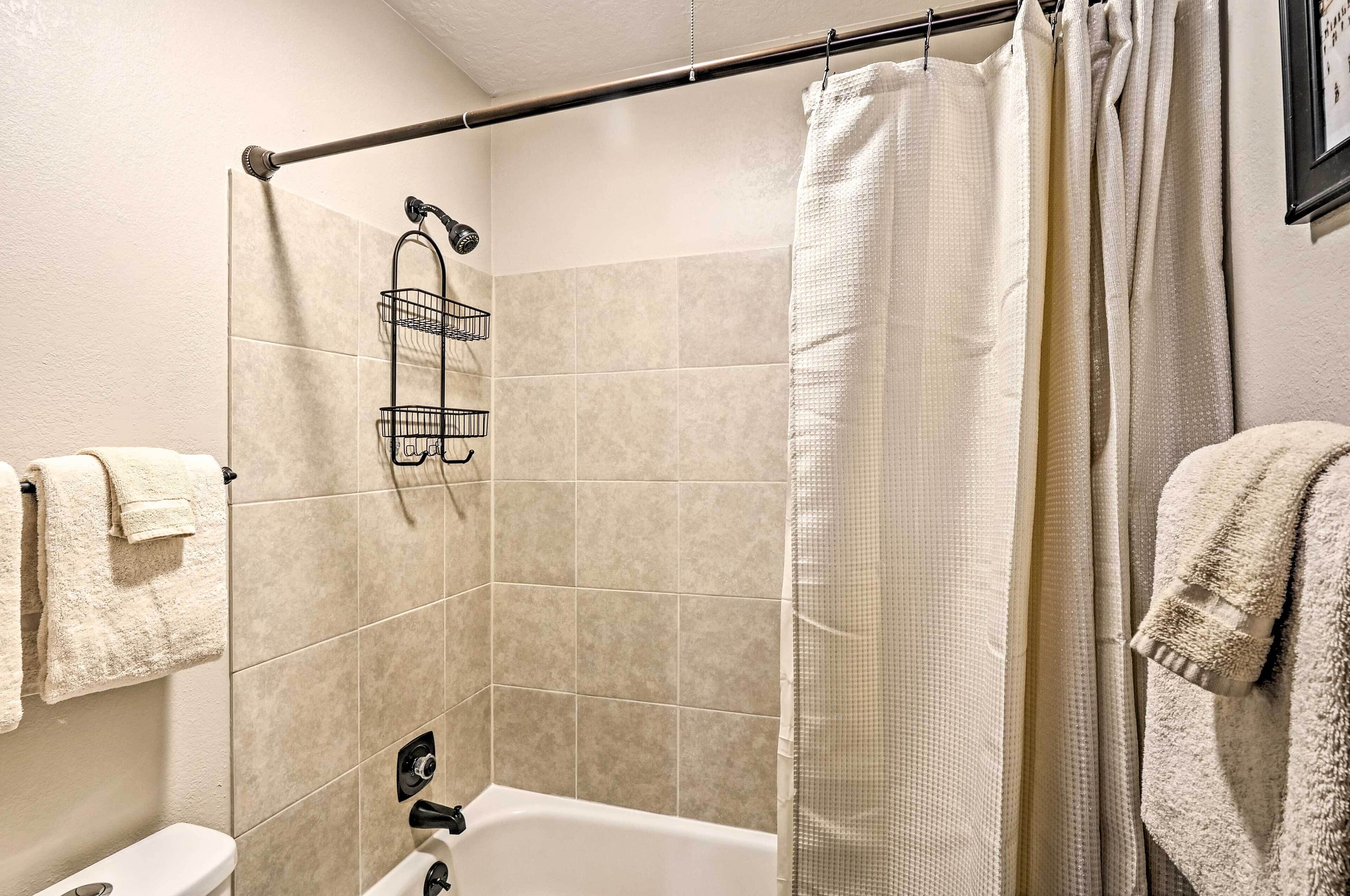 A bathroom with beige tiles, a shower curtain, a towel rack, and a showerhead.