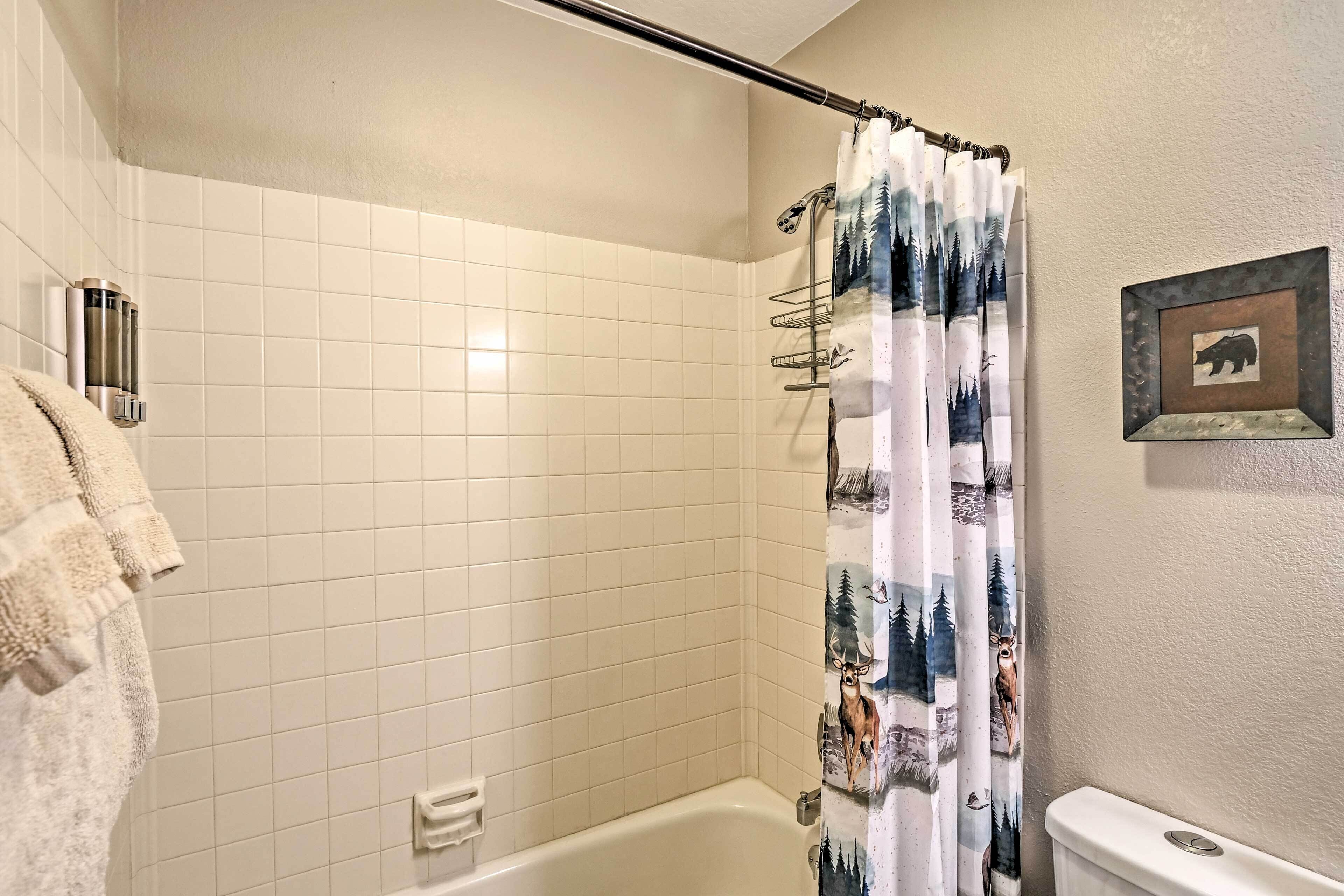 A bathroom with a bathtub, a toilet, and a shower curtain with a forest design.