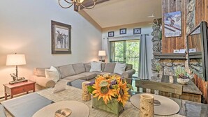 A cozy living room with a sectional sofa, a dining table with a vase of sunflowers, a chandelier, and a stone fireplace wall. - Condo w/ Pool + Hot Tub - Walk to DT Winter Park! (Winter Park)