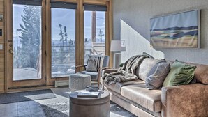 A modern living room with a leather sofa, a coffee table, and a chair. There is a large window with a view of trees and mountains.