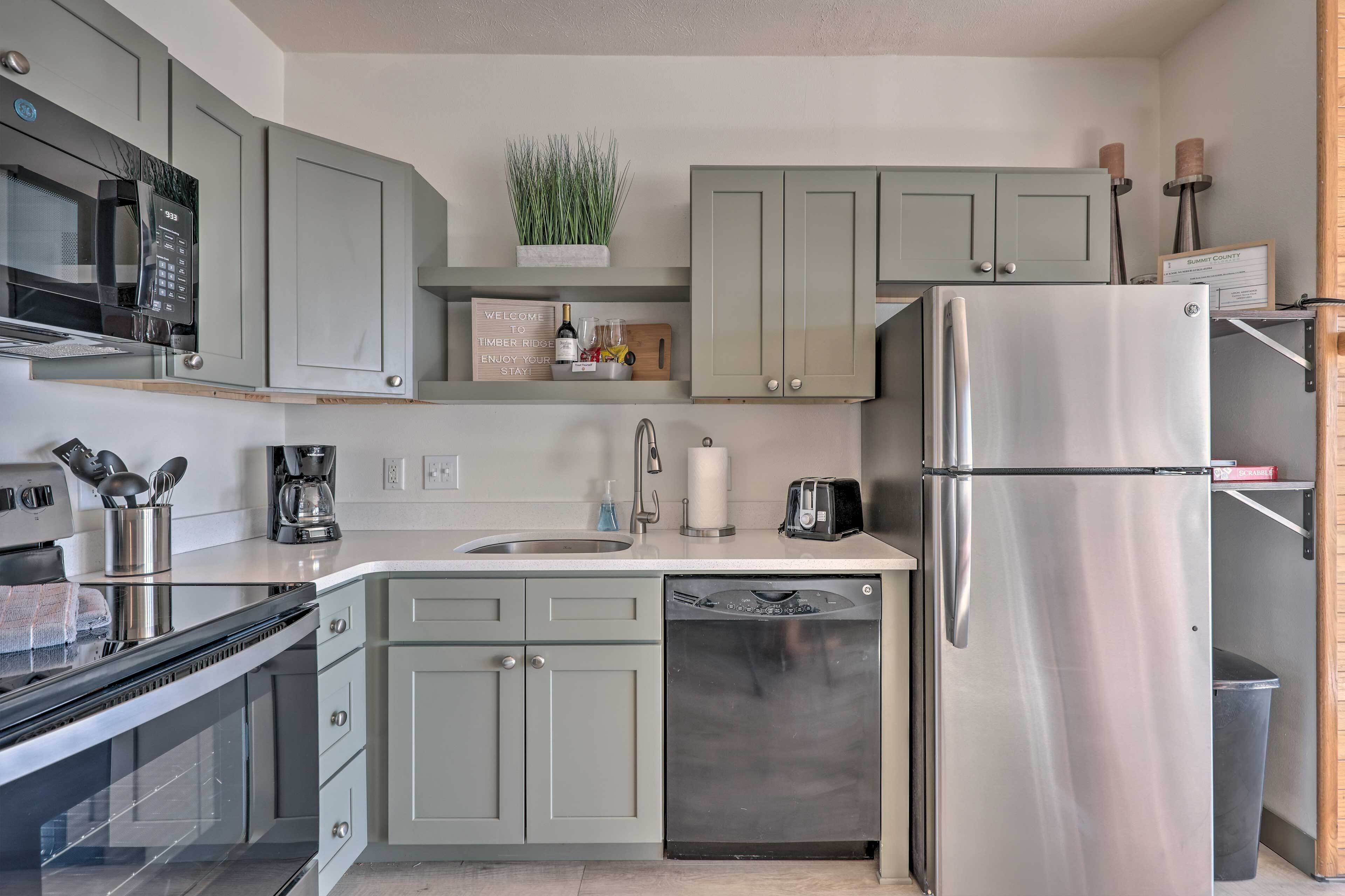 A modern kitchen with grey cabinets, a stainless steel refrigerator, a built-in dishwasher, and a coffee maker.