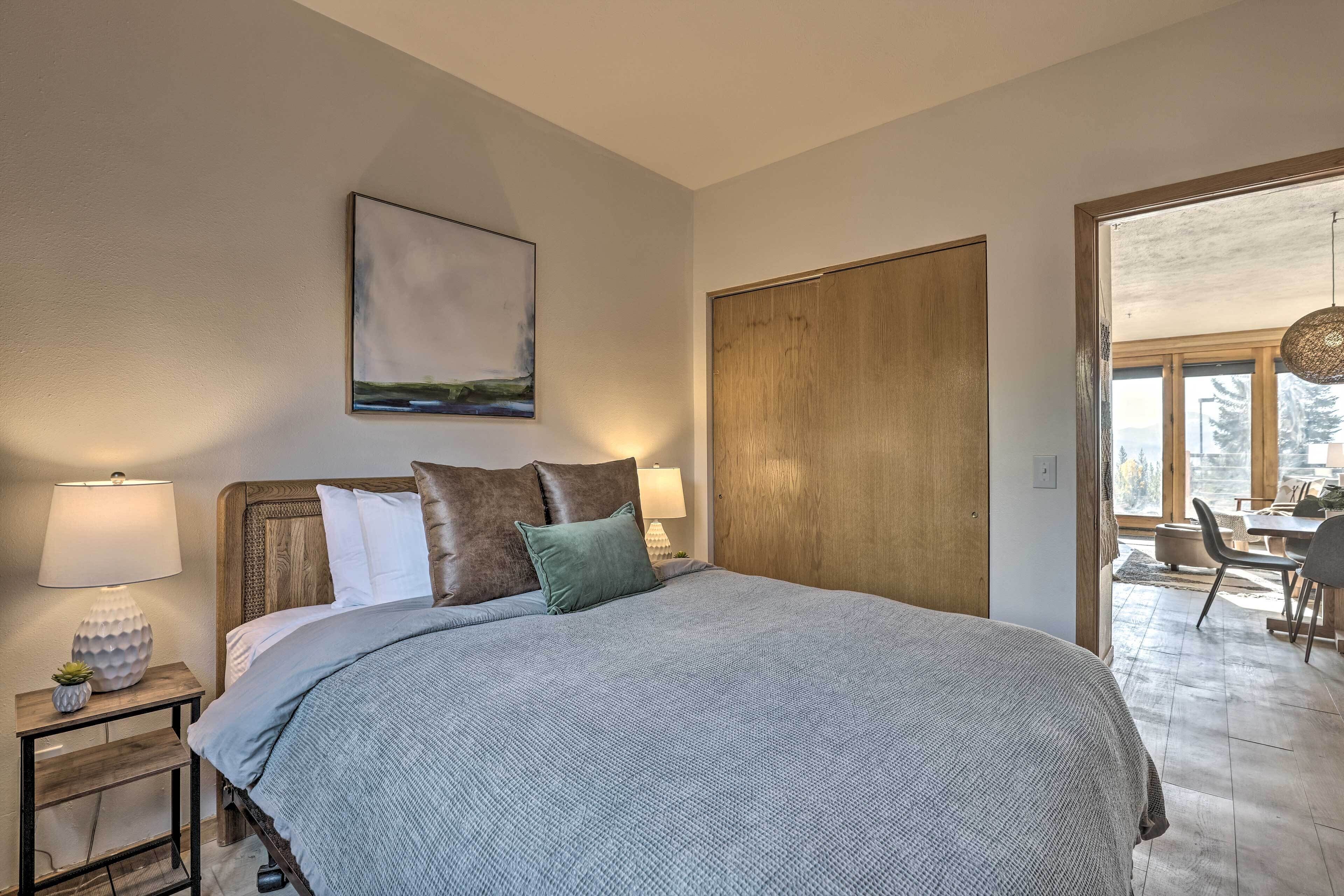Une chambre à coucher avec un grand lit, une table de chevet avec une lampe, un tableau accroché au mur et une porte en bois.