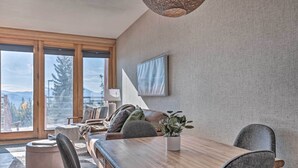 A modern dining area with a wooden table, grey upholstered chairs, and a potted plant.
