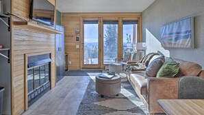A modern living room with a fireplace, a sofa, and a large window offering a view of the outdoors.