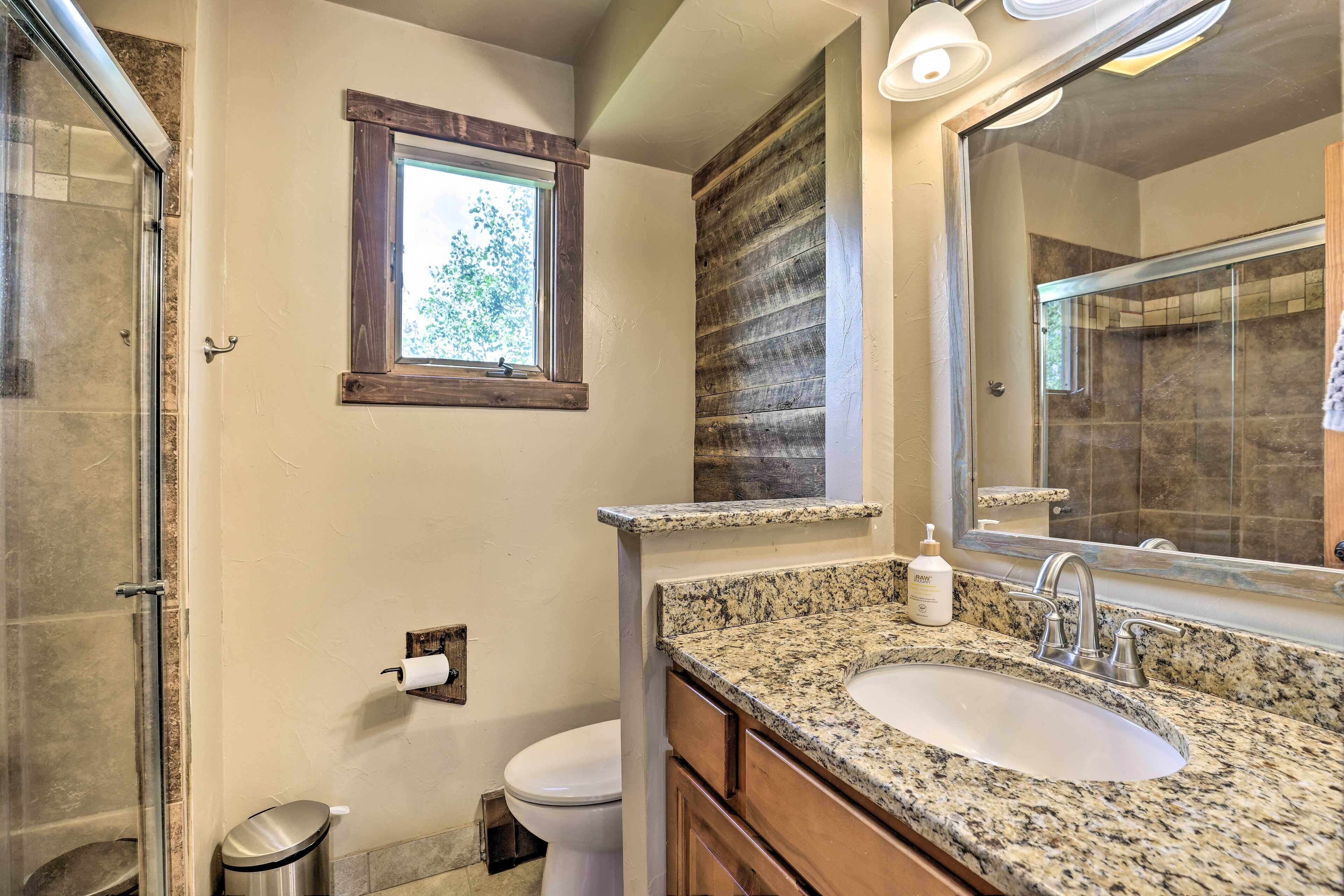 A bathroom with a granite countertop sink, a large mirror, and a window above the toilet.