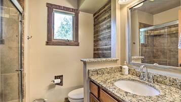 A bathroom with a granite countertop sink, a large mirror, and a window above the toilet.