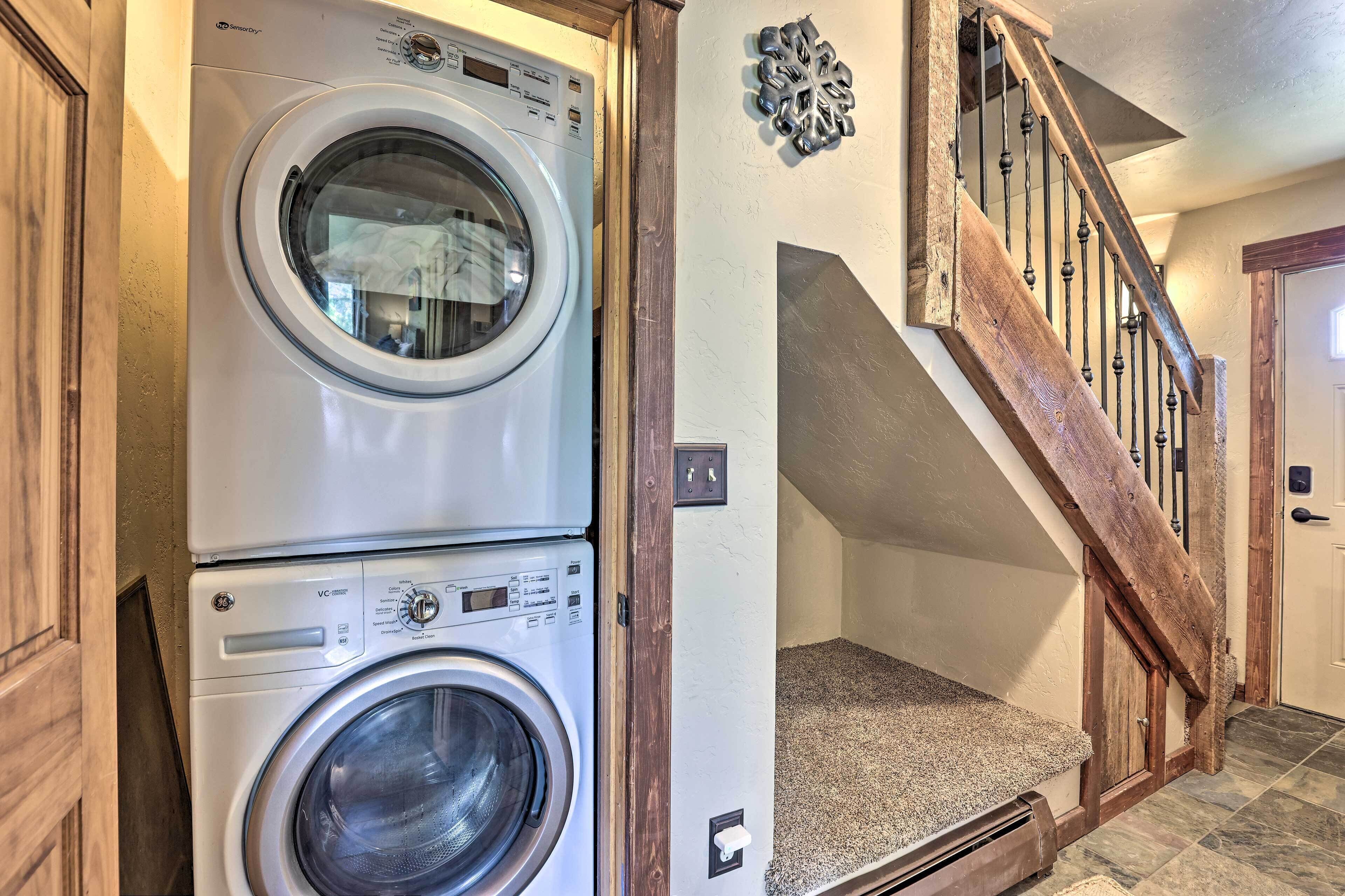A laundry room with stacked washers and dryers, a wooden staircase, and a carpeted landing.