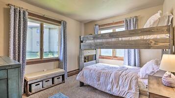 Une chambre avec un lit superposé, un banc doté de tiroirs de rangement, une table de chevet avec une lampe et une fenêtre avec des rideaux.