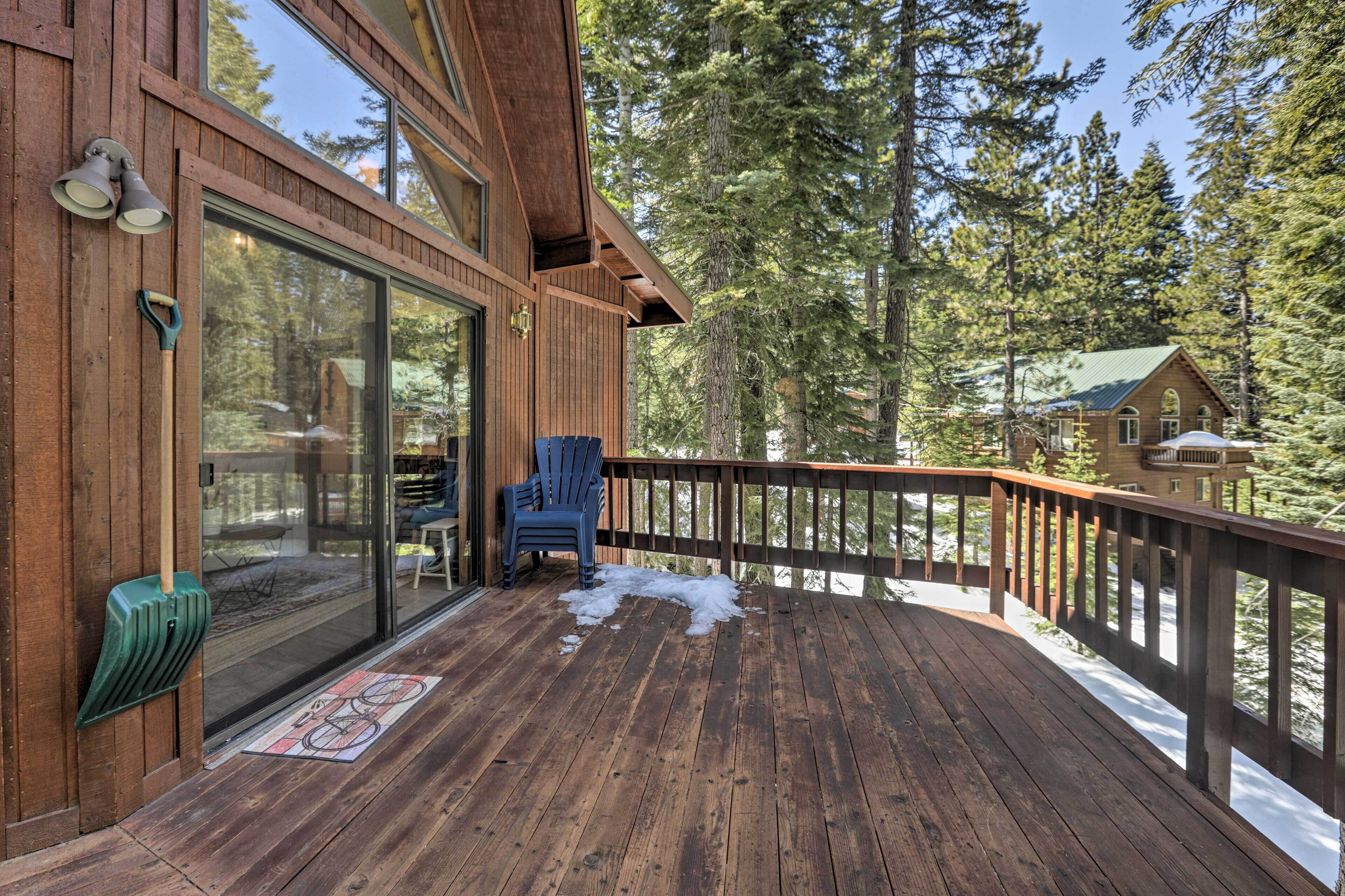 Eine Holzterrasse mit einer Glastür, die zu einem Raum führt, ein blauer Stuhl und verschneiter Boden.