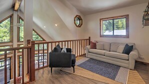 A spacious living area with a wooden staircase, a sofa, and a view of the outdoors through large windows.