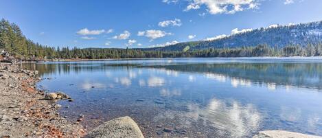 A clear lake with a rocky shoreline and a forested mountain in the background.