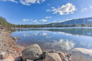 Un lago transparente con costa rocosa y una montaña boscosa al fondo.
