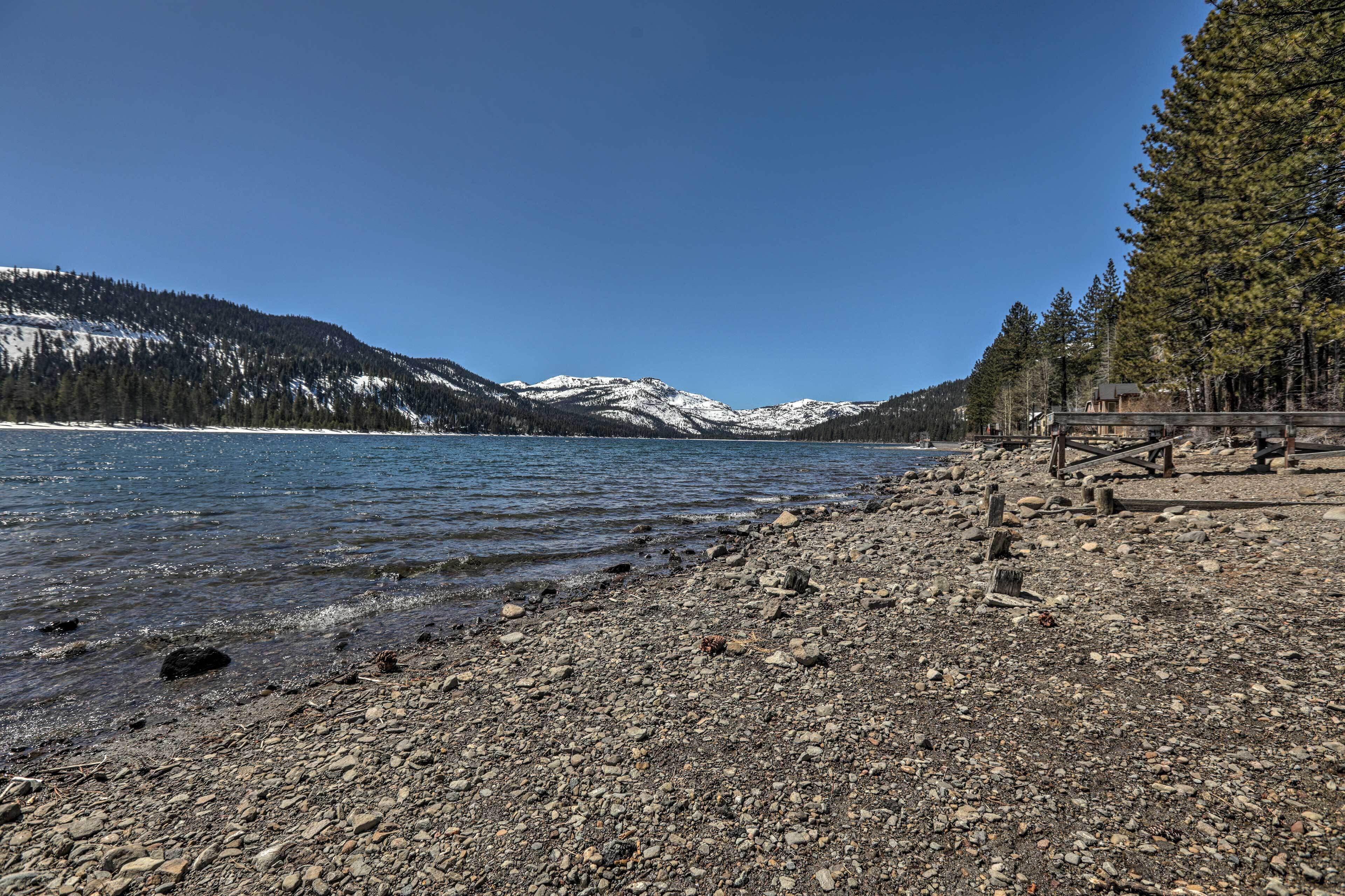 A rocky shoreline with a clear view of a lake and snow-capped mountains in the background.