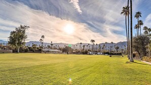 A wide, open grassy field with tall palm trees and mountains in the background. - Trendy Palm Desert Home w/ Patio & Pool Access (Palm Desert)