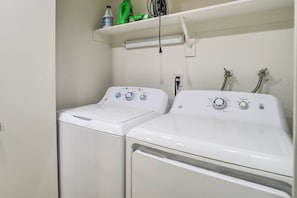 Une buanderie avec deux machines à laver blanches et une étagère au-dessus, où sont rangés les produits de nettoyage.