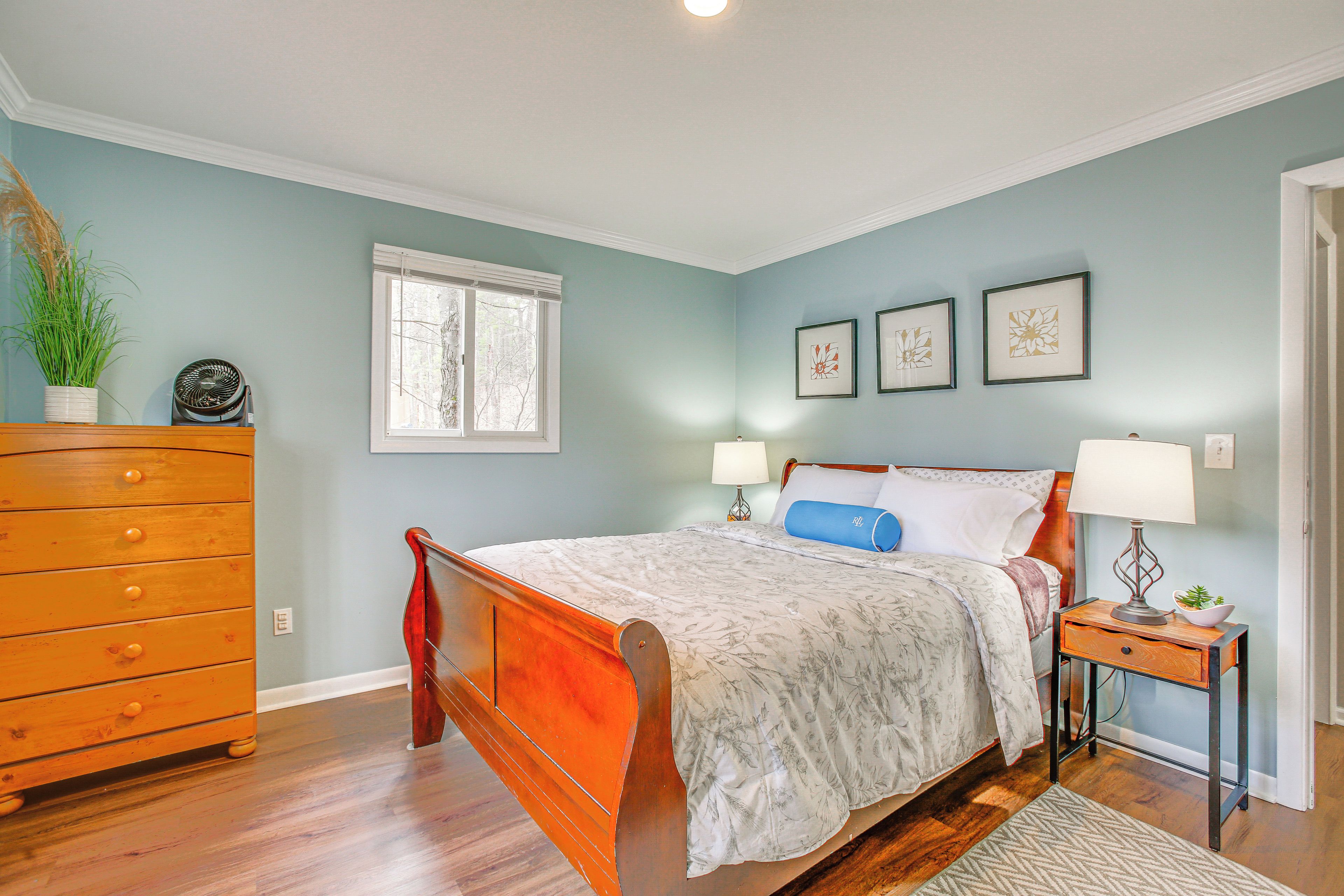 A bedroom with a wooden bed, a dresser, a window, and wall art.