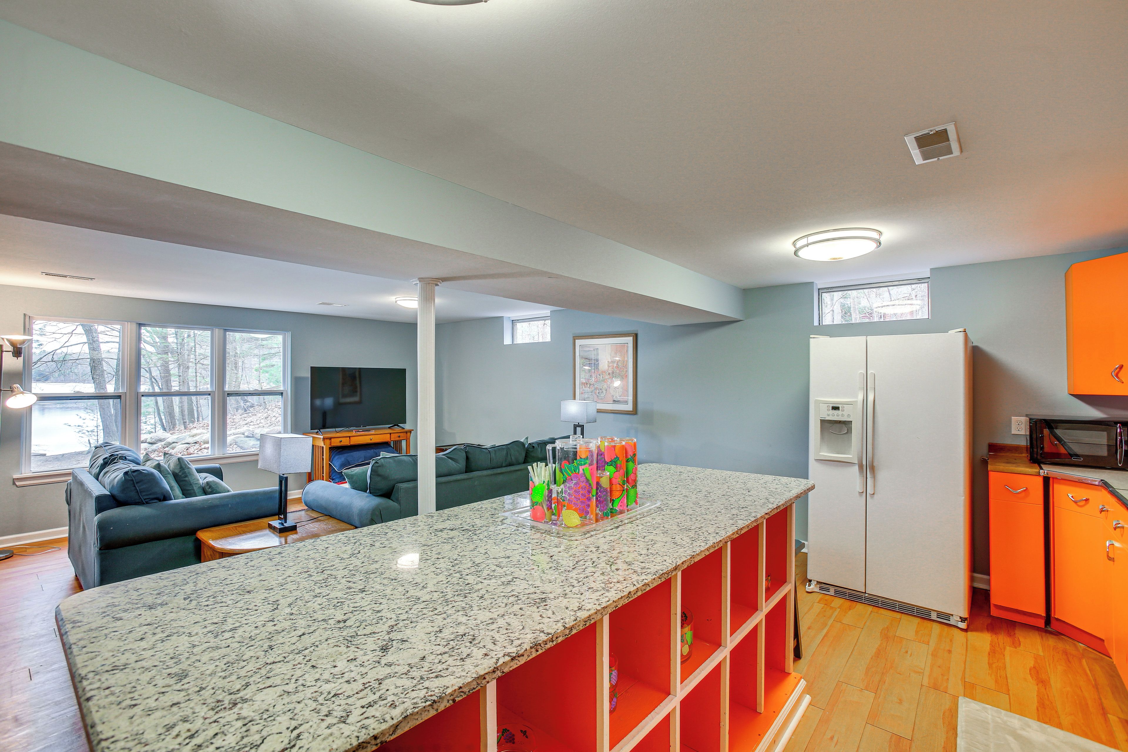 A modern kitchen with a granite countertop, a white refrigerator, and orange cabinets.