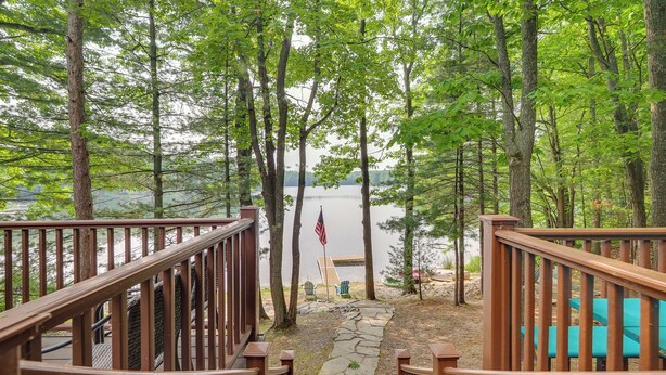 Une terrasse en bois menant à un lac, avec un drapeau, le tout entouré d’arbres.