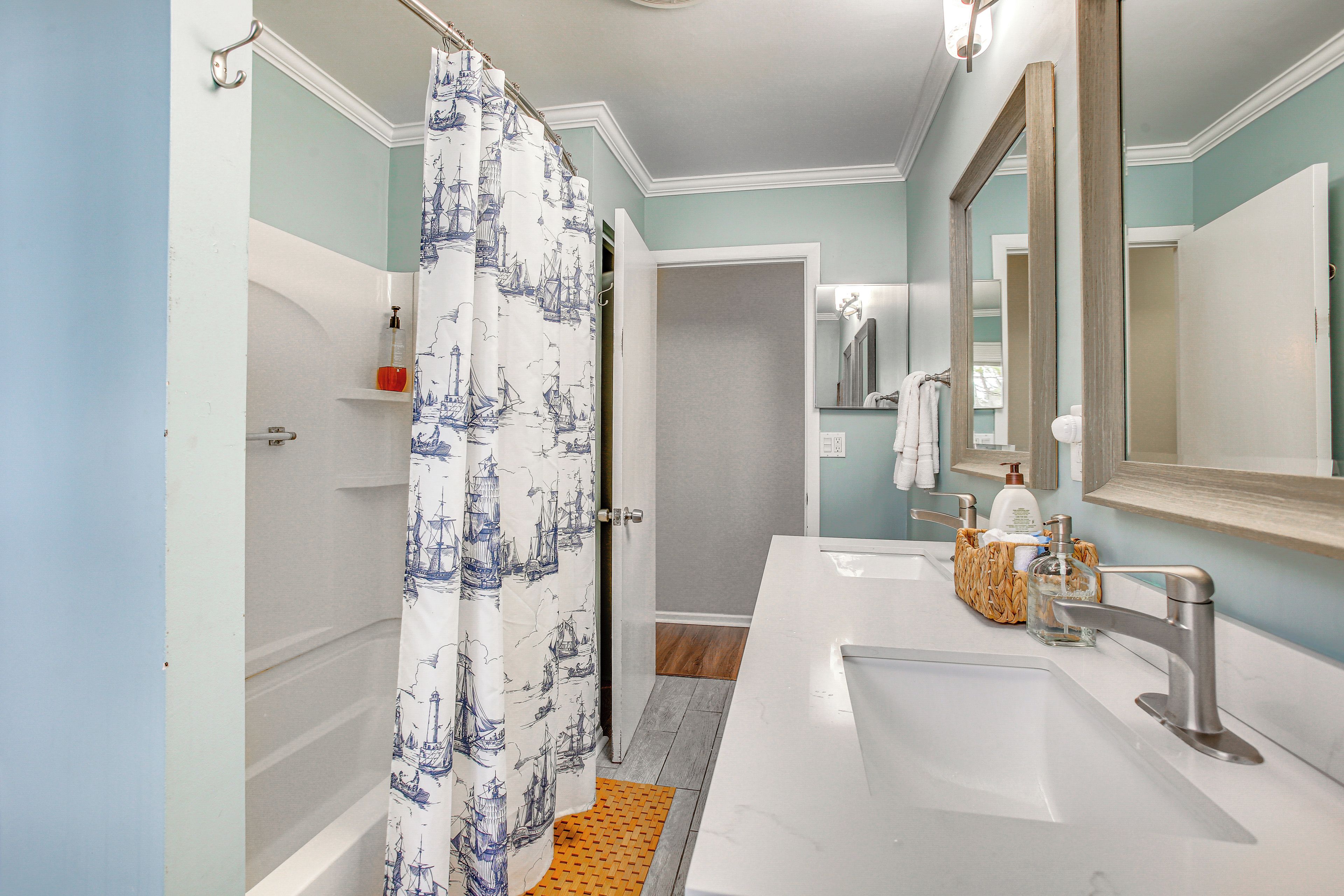 A bathroom with a shower curtain, a sink, a mirror, and toiletries.