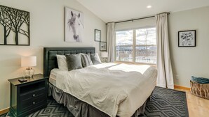 A modern bedroom with a large bed, a nightstand, a window with a view of a snowy landscape, and artwork on the walls. - 8 Mi to Keystone: Mtn-view Ski Retreat! (Silverthorne)