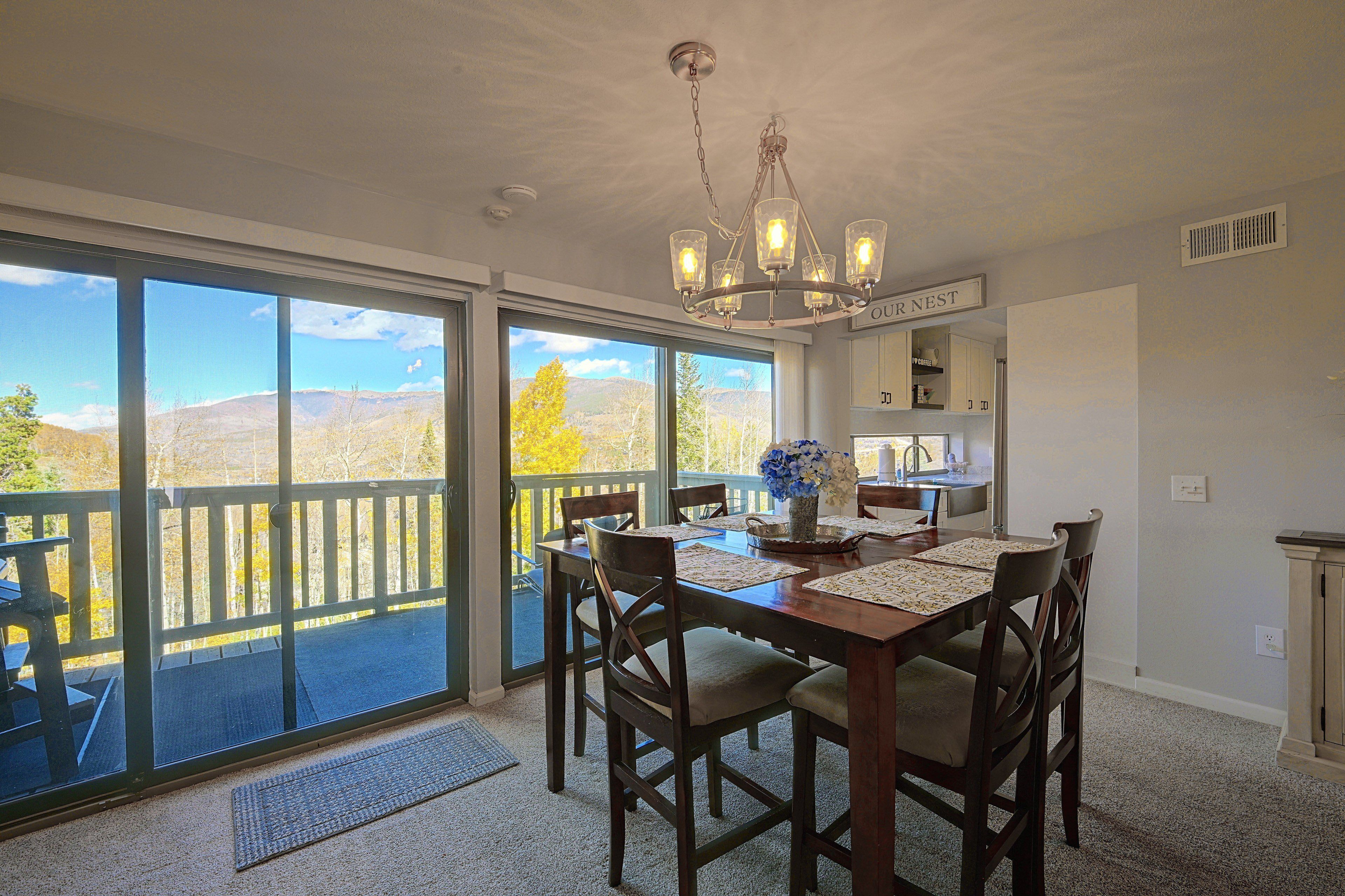 A dining area with a view of mountains, a chandelier, and a sign reading 'OUR NEST'.