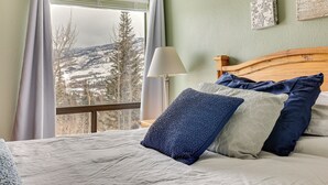 A bedroom with a large window, a wooden headboard, and multiple pillows. - Ski, Shred & Tube: Mtn-view Condo in Silverthrone! (Silverthorne)