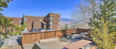 Un bâtiment moderne doté d’une terrasse en bois, de tables de pique-nique et offrant une vue sur les montagnes.