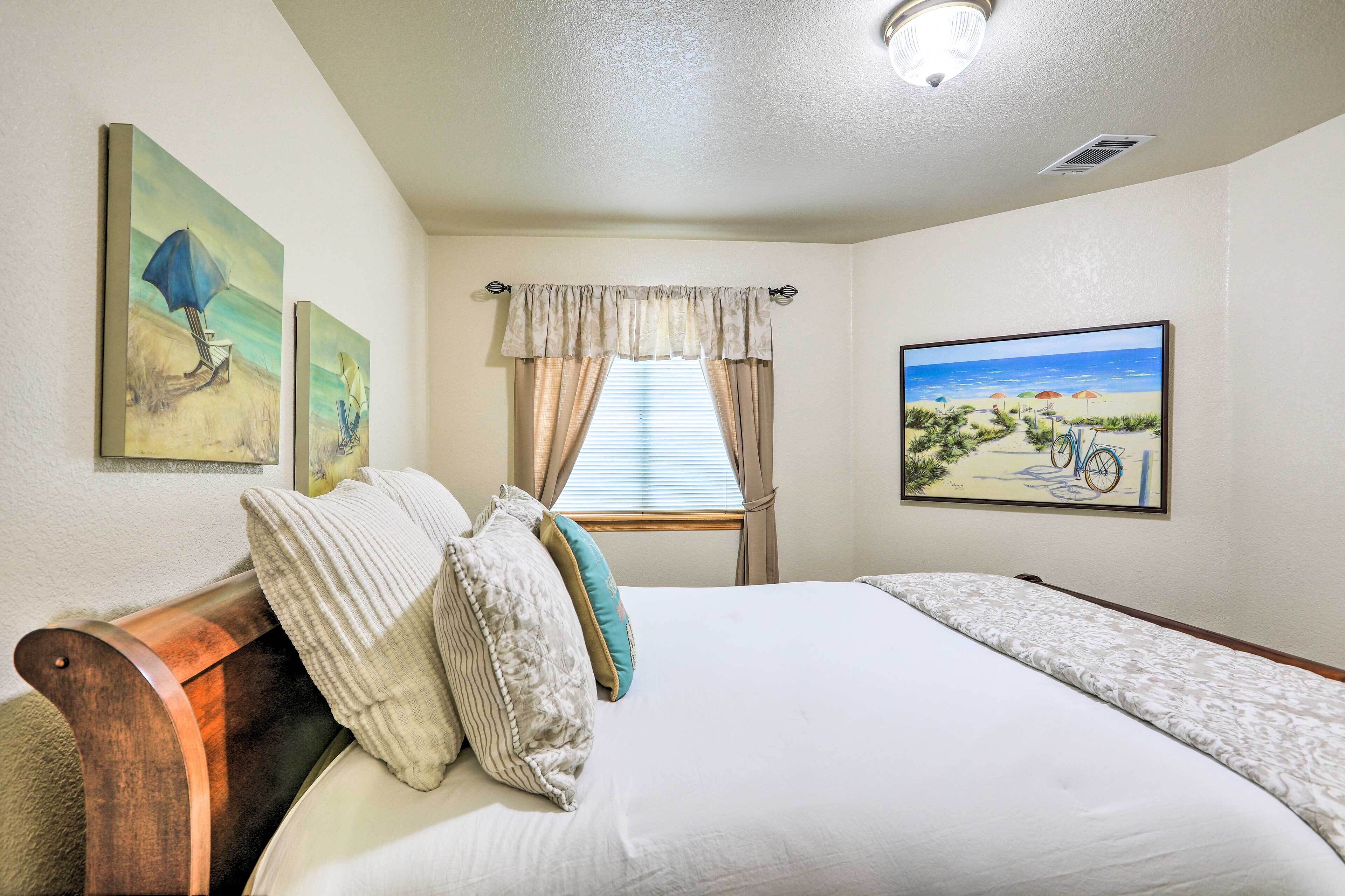 A bedroom with a bed, a window with curtains, and two paintings on the wall.