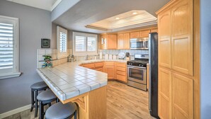 A kitchen with wooden cabinets, a stainless steel refrigerator, and a tiled island with stools. - Ideally Located Ocean Escape Near Beach & Wineries (Grover Beach)