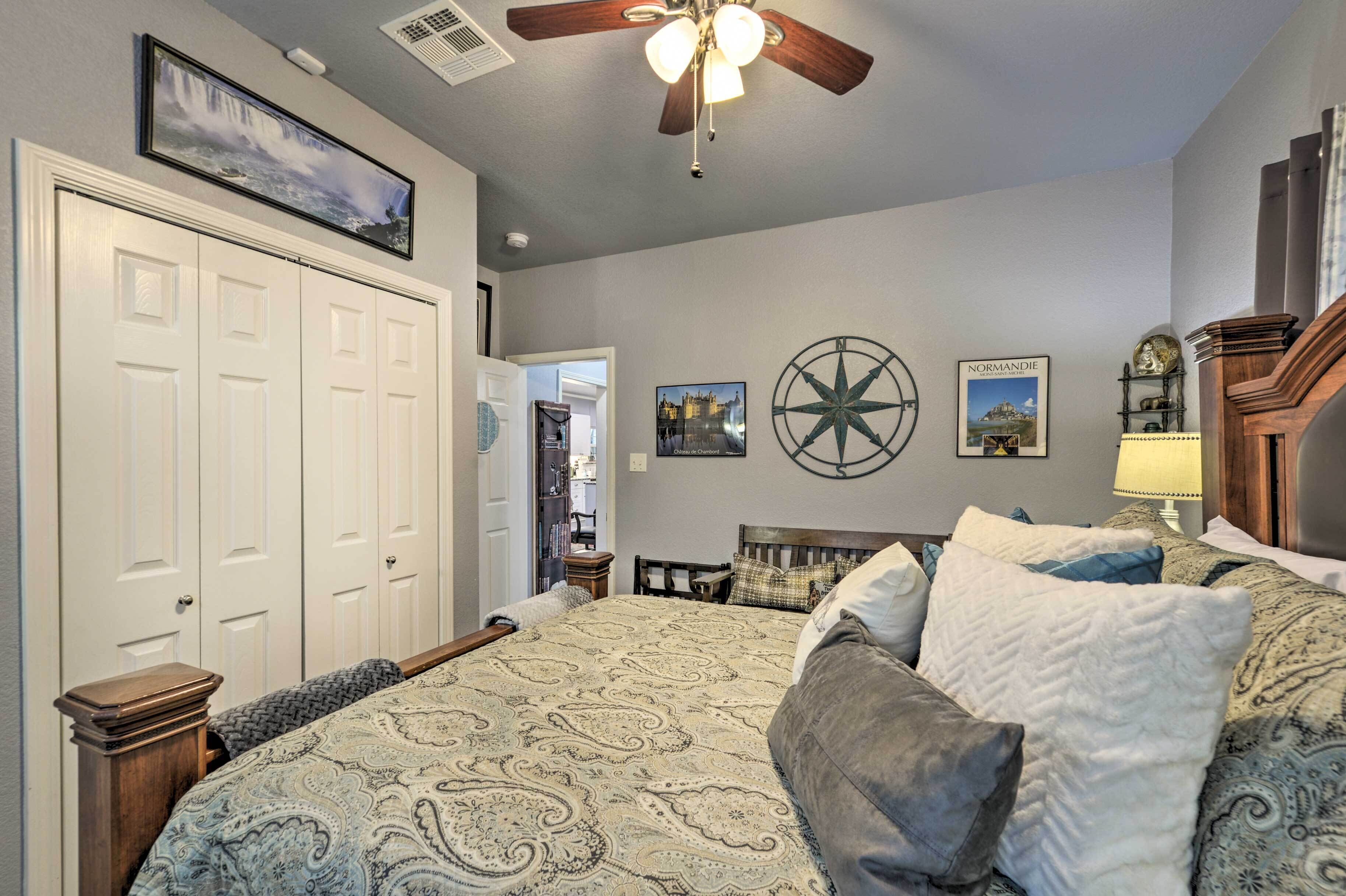 A bedroom with a large bed, a ceiling fan, a wall clock, and a framed picture of a castle.