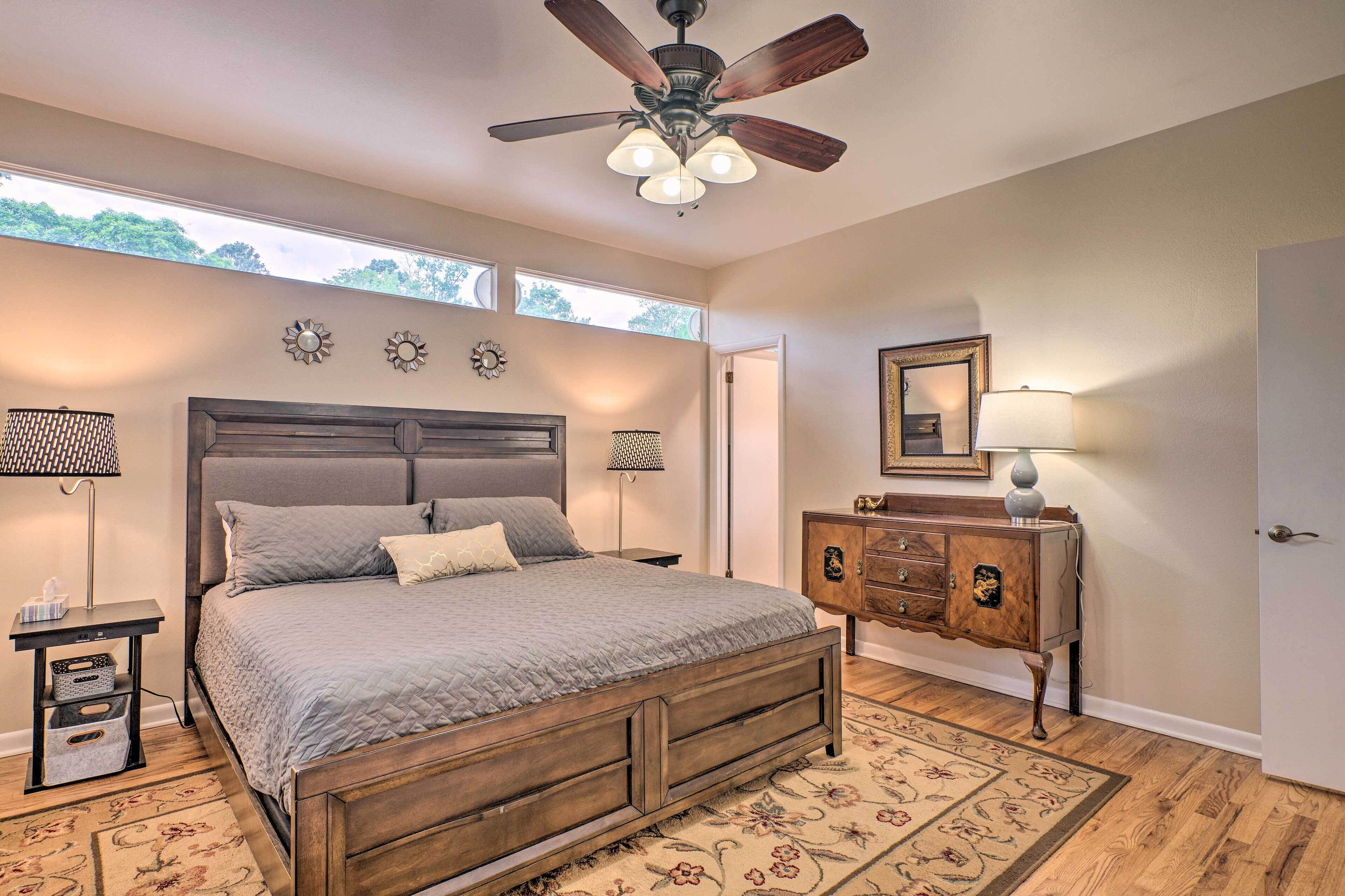 A bedroom with a wooden bed, a ceiling fan, a nightstand with a lamp, a dresser, and a floral rug.