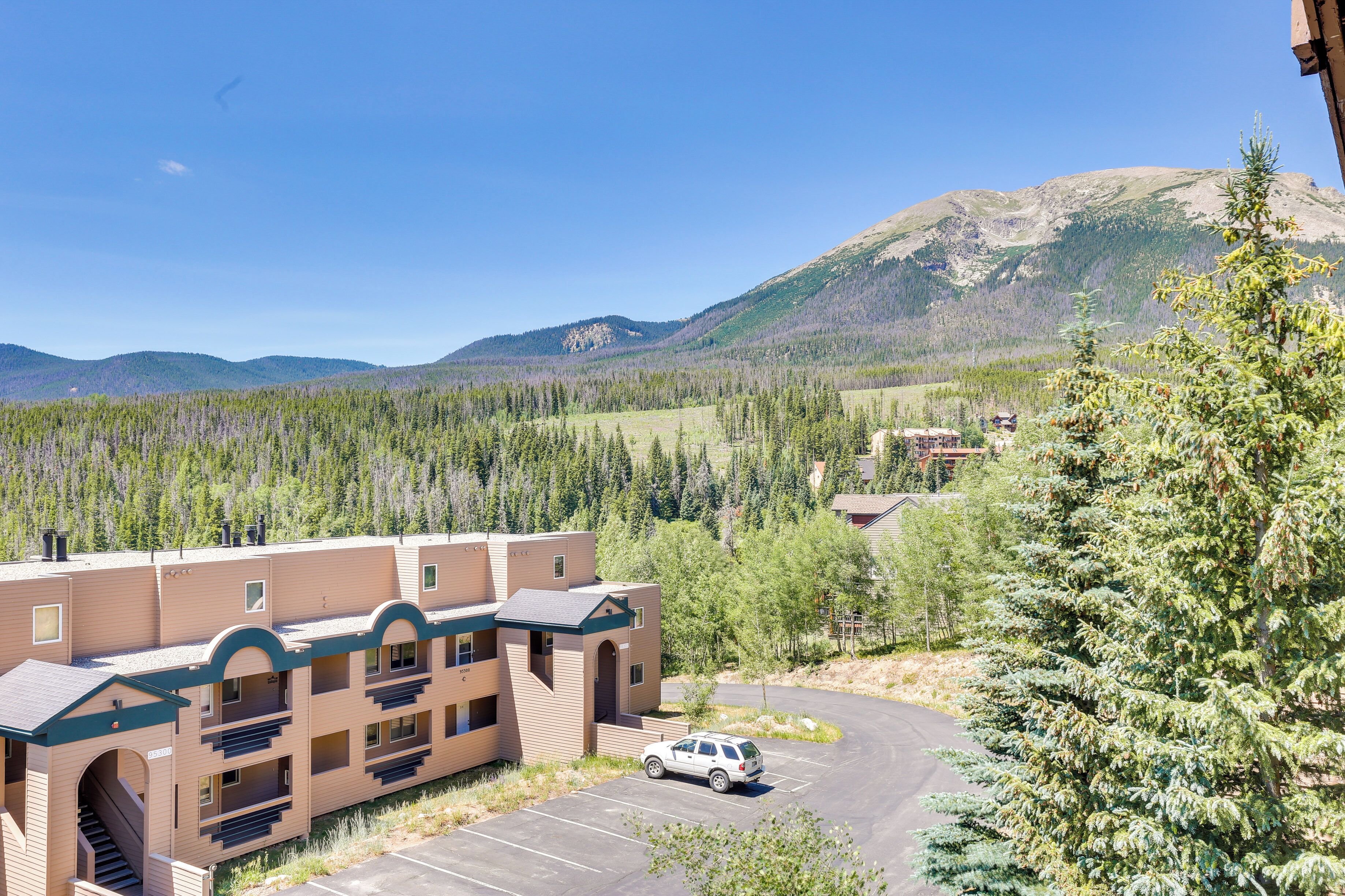 A multi-story building with a parking lot and a view of a forested mountain range.