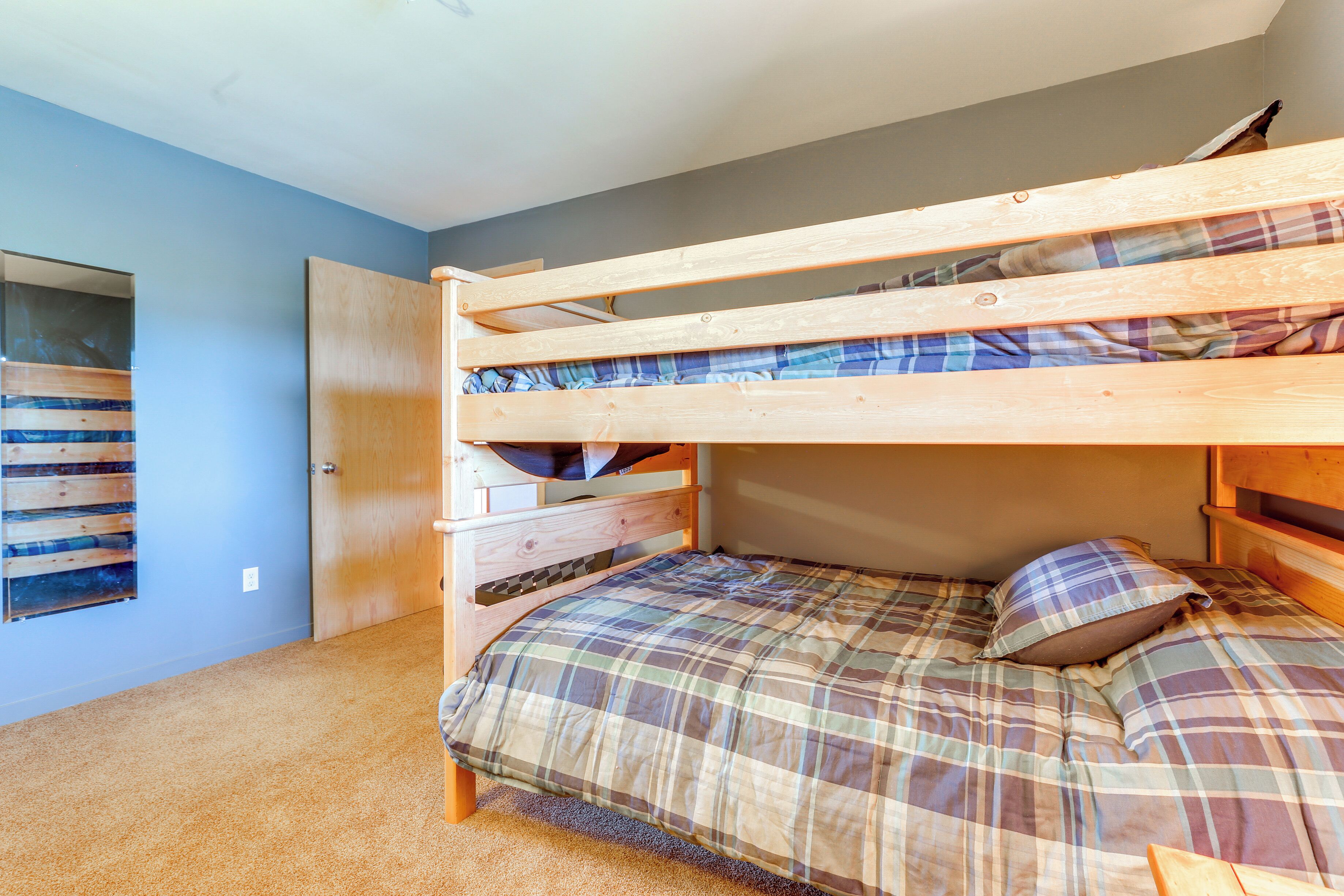 A bunk bed with a plaid bedspread and pillows, a wooden headboard, and a small wooden dresser.