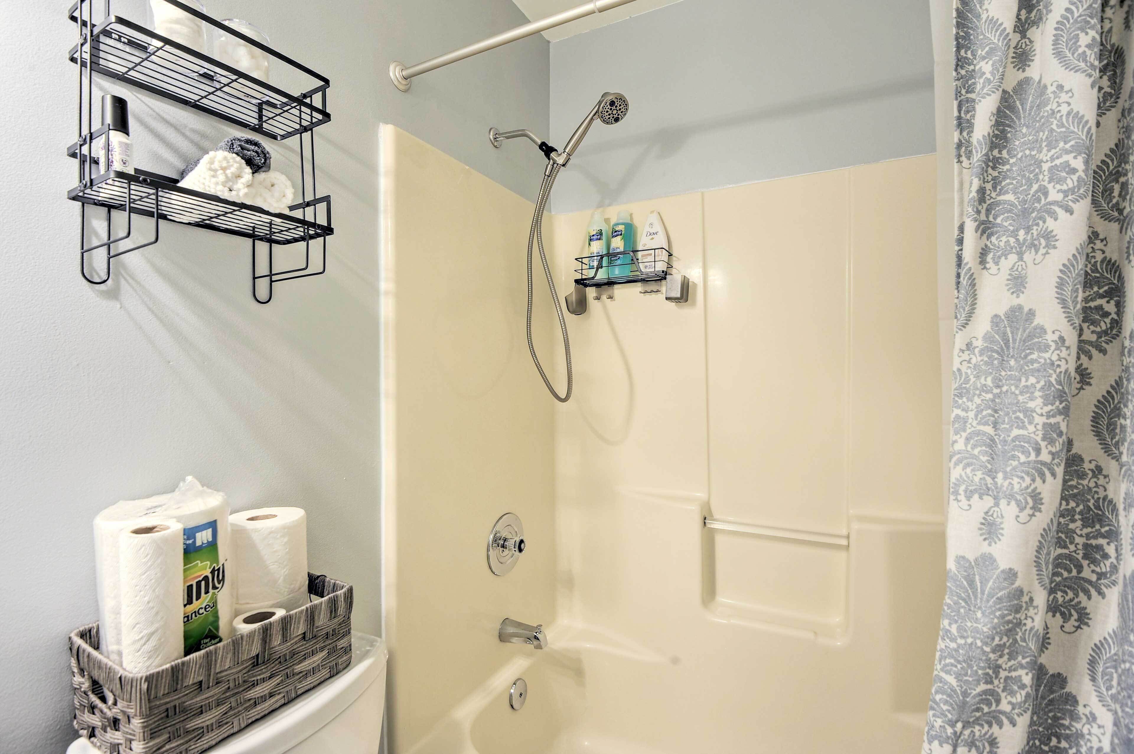 A bathroom with a shower, toilet paper, and toiletries on shelves.