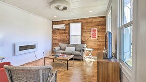 A living room with a wooden wall, a gray sofa, a coffee table, and a TV mounted on the wall. - Contemporary San Antonio Home w/ Private Yard (San Antonio)