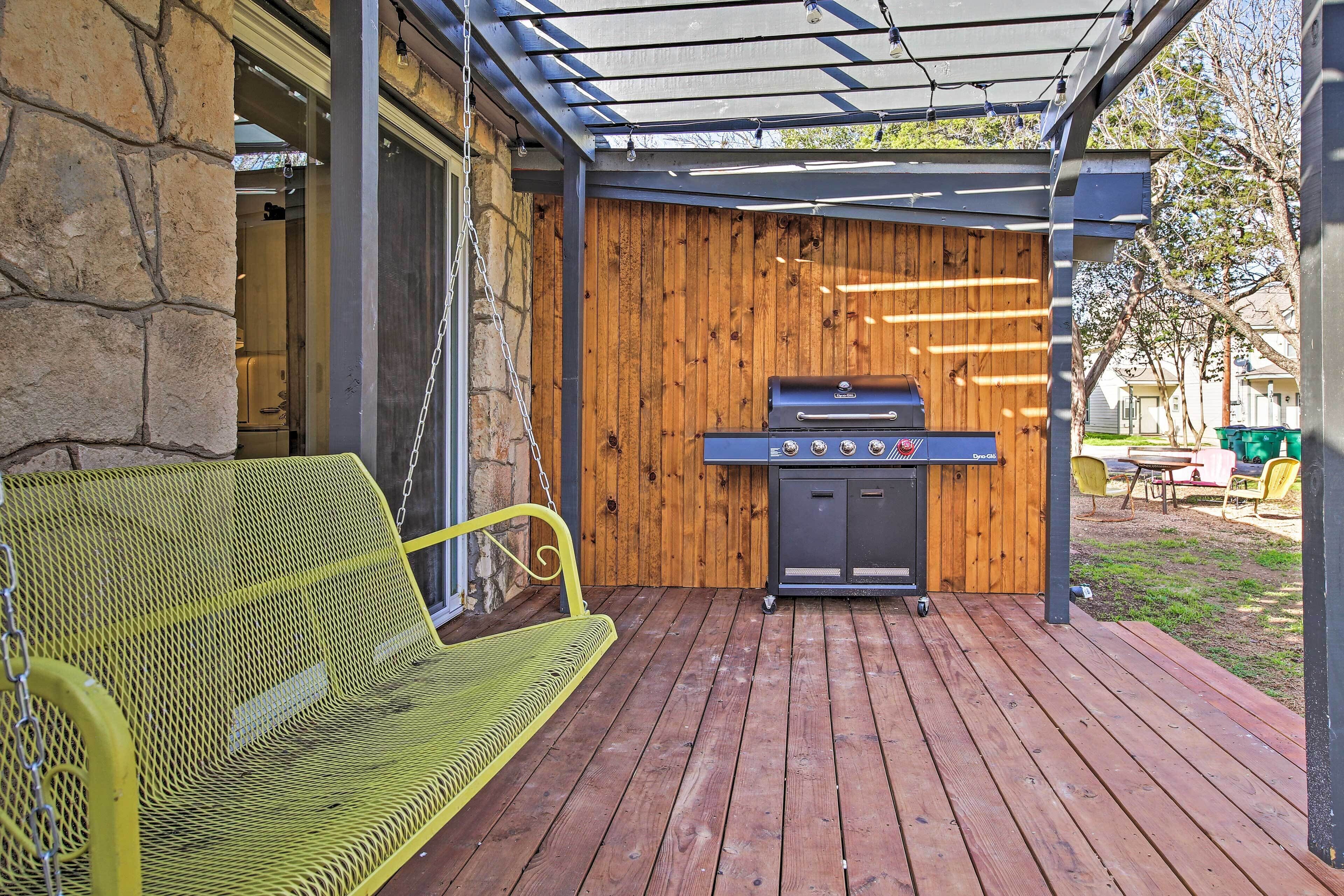 A covered patio with a grill, a yellow metal bench, and a stone wall.
