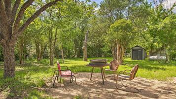 An outdoor seating area with a table and two chairs, surrounded by trees and a shed.