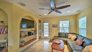 A living room with a sofa, a coffee table, a TV mounted on the wall, and a ceiling fan. - San Antonio House w/ Private Pool, Spa & Grill (San Antonio)