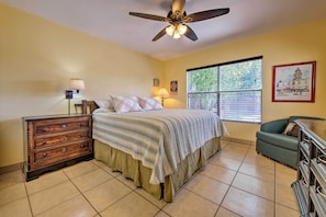 Quarto com cama, penteadeira, mesa de cabeceira, abajur, janela e obra de arte.
