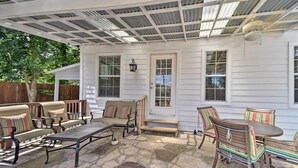 A covered patio with stone flooring, outdoor furniture, and a white house with windows and a door. - San Antonio House w/ Private Pool, Spa & Grill (San Antonio)