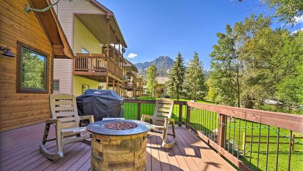 Une terrasse en bois avec un foyer en pierre, des sièges d’extérieur et une vue sur les montagnes.