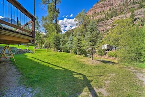 A well-maintained grassy area with a wooden deck and a stone wall, surrounded by trees and a mountain backdrop.