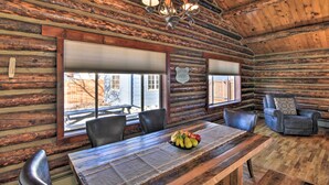 L’intérieur d’une cabane en rondins, avec une table à manger, des chaises, un lustre et une cheminée.