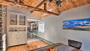 Un coin repas avec une table en bois, un panier de fruits et un tableau représentant des montagnes accroché au mur.