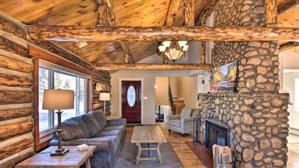 L’intérieur d’une cabane en rondins, avec une cheminée en pierre, des poutres en bois au plafond, un canapé et une table à manger.