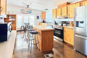 A modern kitchen with wooden cabinets, a stainless steel refrigerator, and a bar area with stools.