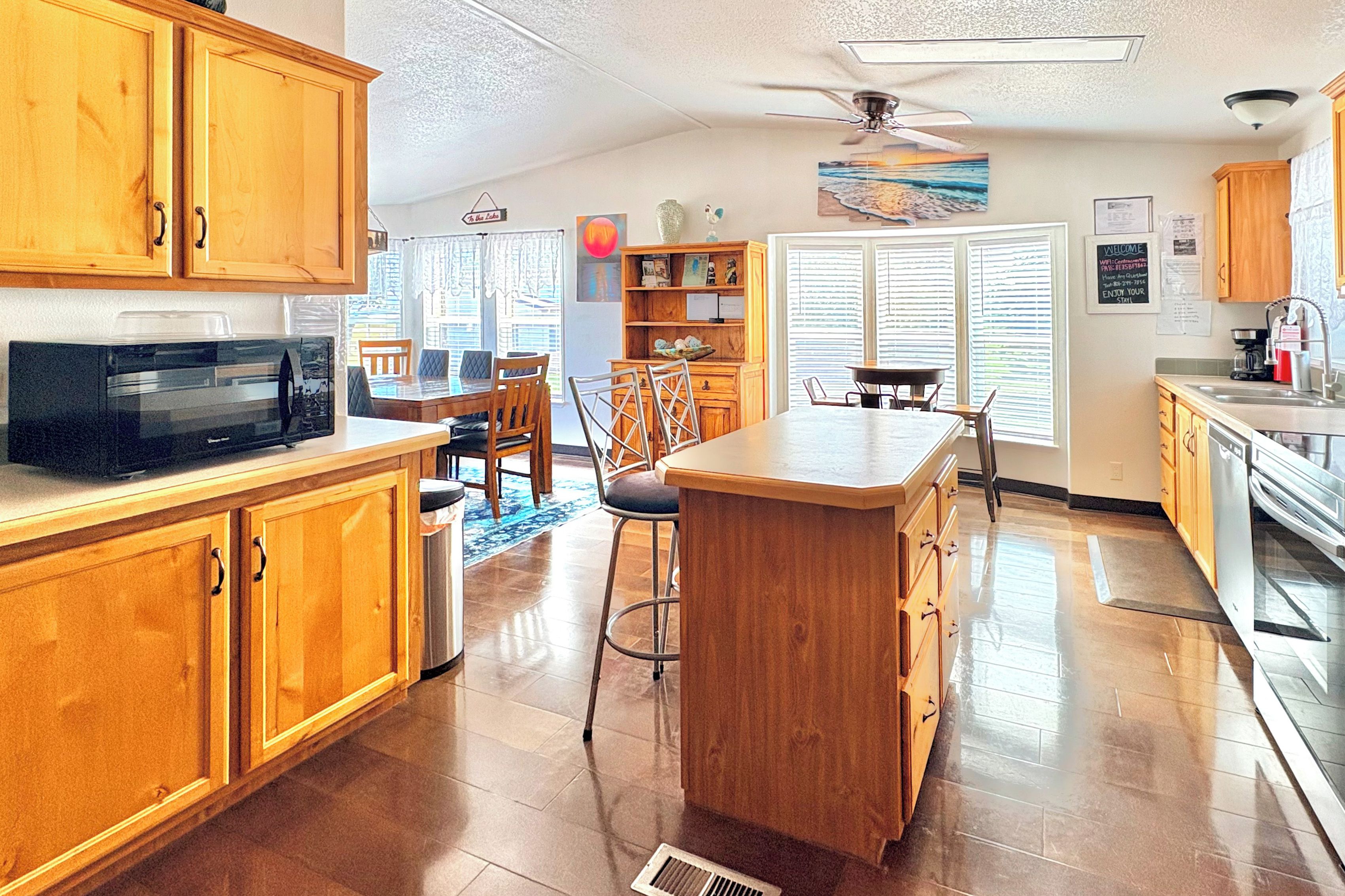 A kitchen with wooden cabinets, a microwave, a dining area with chairs, a bar stool, and a ceiling fan.