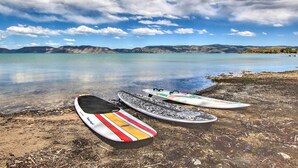 Kolme surffilautaa rannalla, jossa vesi on kirkasta ja taustalla näkyy kaukaisia vuoria.
