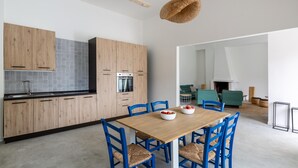 A modern kitchen with wooden cabinets, a built-in oven, and a dining area with a wooden table and blue chairs. - 3320 Villa Fiorezza - 3 PT by Barbarhouse (Maruggio)
